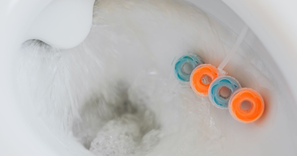 From above of flushing water in toilet bowl with cleaner and freshener block