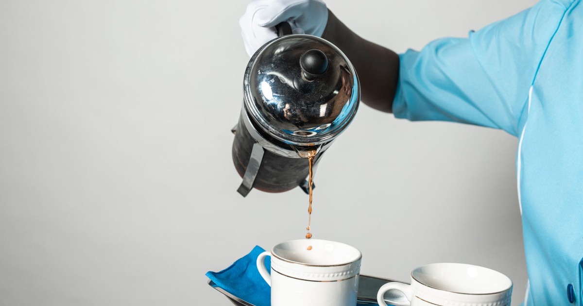 Close-up of a person serving coffee from a French press into cups, showcasing hospitality.