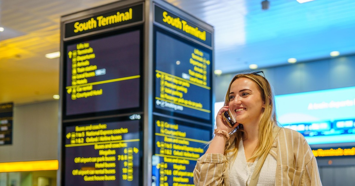 Smiling woman on phone in South Terminal of Gatwick Airport, Horley, enjoying her travel experience.