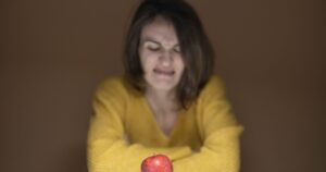 The 22 Most Hated Foods in America, Ranked by Real Data A woman in a yellow sweater shows disgust while looking at a fresh red apple on a table.