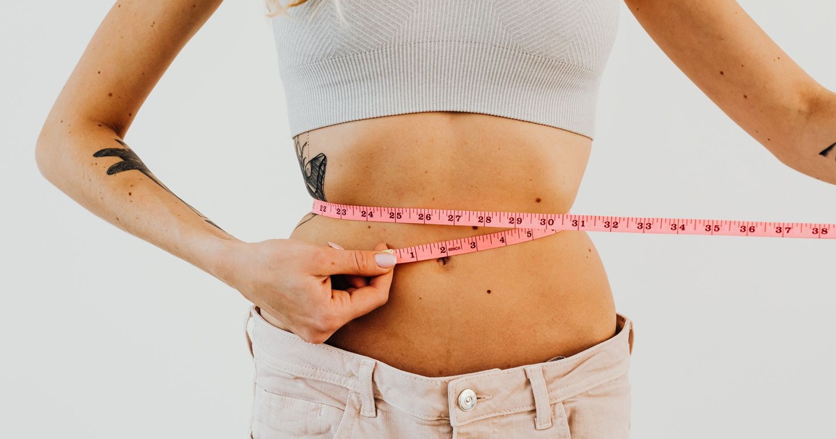 Close-up of woman in sports bra measuring waist with pink tape for fitness goals.