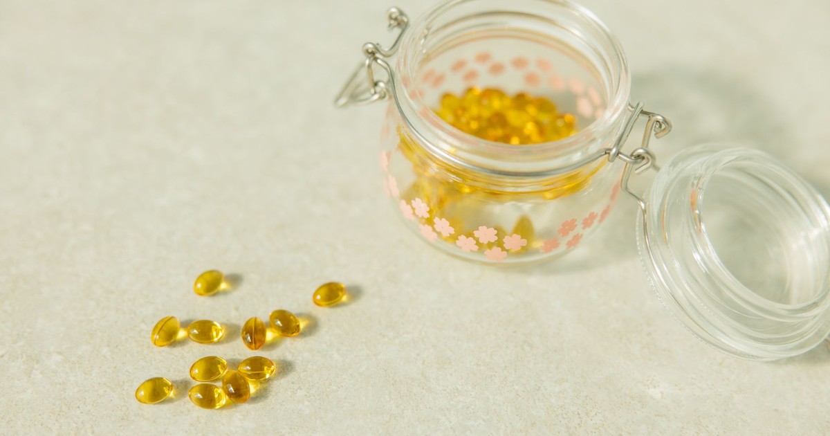 Close-up of open glass jar filled with yellow health capsules on light surface.