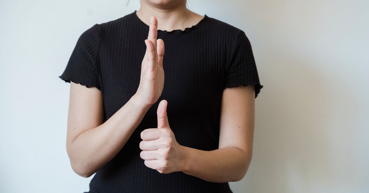 Close-up of a person in black attire making hand gestures against a white background.