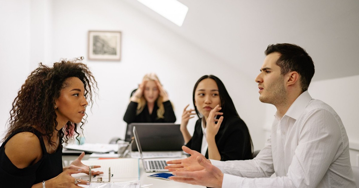 A multi-ethnic team engaged in a heated office discussion, displaying various emotions.