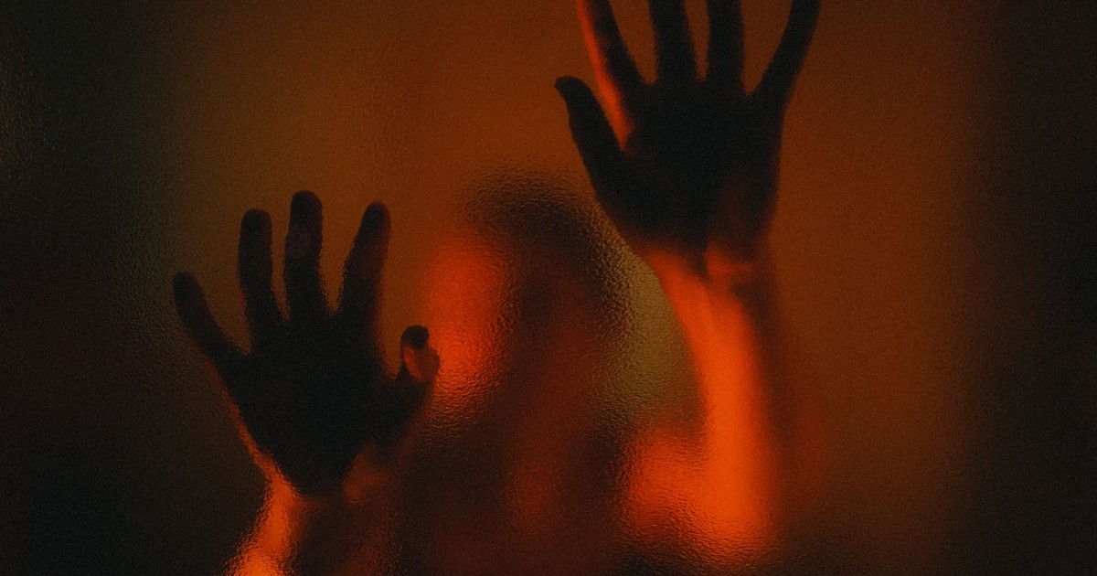 Mysterious silhouette of hands on frosted glass with dramatic red lighting.