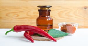 Pharmacy bottle with red chili pepper extract (tincture, infusion, oil) and fresh chili pepper pods. Baldness, alopecia natural remedy and pain relief. Copy space.