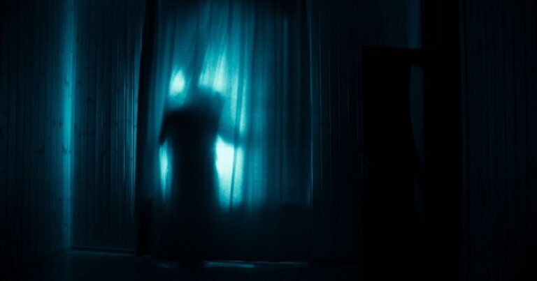 Horror silhouette in window with curtain inside bedroom at night. Horror scene. Halloween concept. Blurred silhouette of ghost
