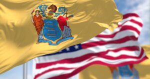 State Is Set to Charge Companies With Workers on Medicaid. Other States May Follow The New Jersey state flag waving along with the national flag of the United States of America. In the background there is a clear sky. New Jersey s a state in the Northeastern regions of the US