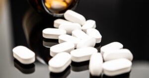 A 20-Minute Sound Wave Procedure Just Ended One Man's Opioid Addiction Close-up image of white opioid pills spilled from a dark amber prescription bottle onto a reflective surface, highlighting the dangers of opioid overdose and misuse.