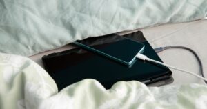 Smartphone and tablet computer are charging in bed under a pillow and blanket. Concept of overheat and fire hazard.