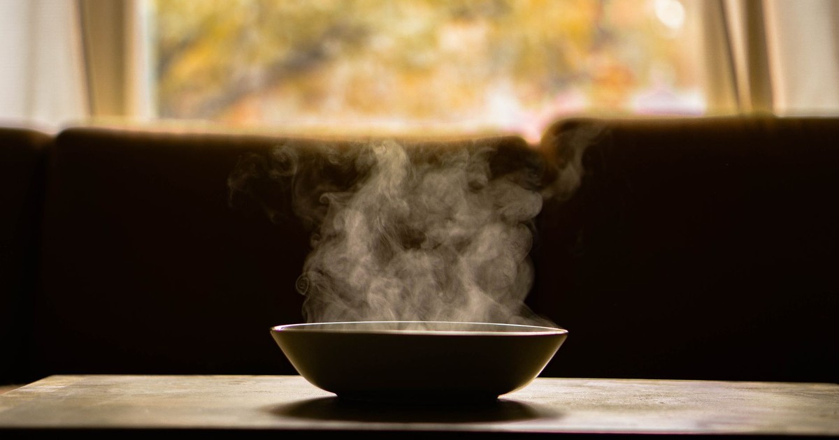 A steaming bowl of soup on a wooden table indoors with soft autumn light through a window.