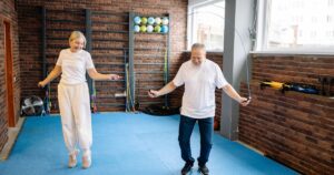 Elderly man and woman joyfully jump rope in a bright gym promoting a healthy lifestyle.
