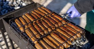 9 in 10 Americans Don't Know Hot Dogs Are Linked to Cancer Sausages being grilled outdoors on a barbecue with charcoal.