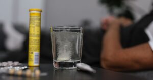 Effervescent tablet dissolving in glass, surrounded by medications, provides a healthcare-focused scene.