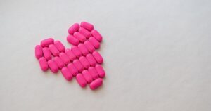 Creative arrangement of pink pills in a heart shape on a white background, symbolizing health and love.