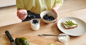 One Avocado a Day May Help Reduce Cholesterol in Adults with Obesity A person prepares a healthy breakfast with yogurt, blueberries, and avocado toast.