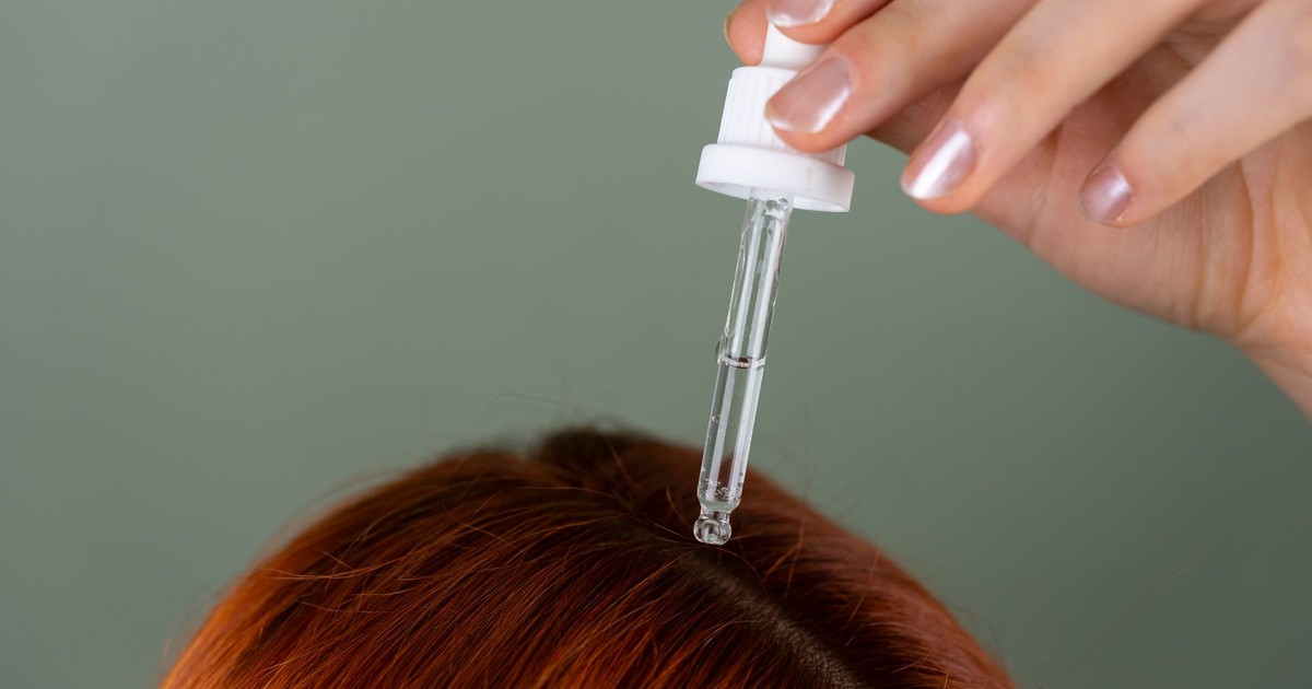 Close-up of applying serum to roots with a precision dropper on red hair, showcasing hair care routine.