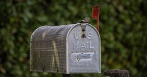 A traditional U.S. mailbox with red flag against a lush green blurred background.