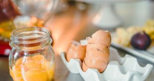 Why Do Egg Yolks Range in Color? Science Has a Surprisingly Simple Answer Cracked brown egg shells and yolks in a glass jar on a kitchen counter.