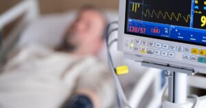 A Blood Test Already in Your Chart Could Predict Heart Attack Survival Patient in hospital bed with heart monitor showing blood pressure and heart rate.