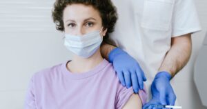 Neurologists Warn Ozempic May Accelerate ALS Progression Tenfold A healthcare worker gives a vaccine injection to a masked patient, wearing gloves.