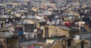 An aerial view of rooftops covered with satellite dishes in a densely populated urban area in India.