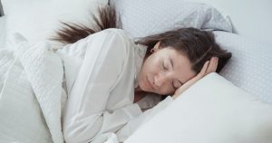 A serene woman rests comfortably in bed with soft pillows and blankets, embracing relaxation.