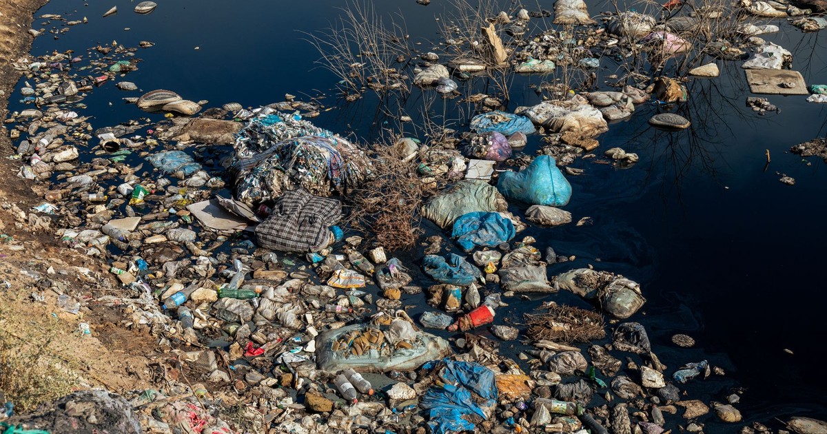An aerial shot of a polluted riverbank covered with plastic waste and debris highlighting environmental issues.
