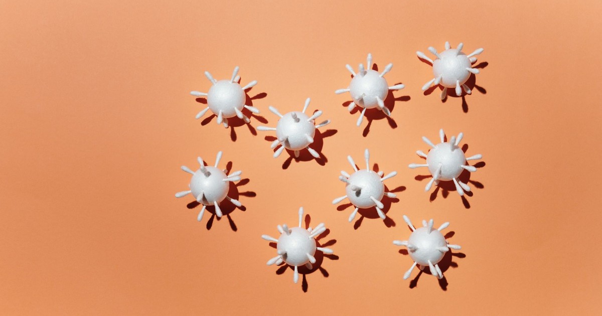 White 3D virus scale models arranged on a peach background, casting shadows.