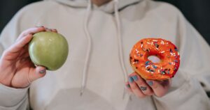 9 Colon Cancer Foods: What to Eat and What to Avoid, Backed by Science Crop unrecognizable female in loose hoodie showing healthy green apple and sweet delicious donut