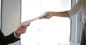 The 4 Words in Your Job Description That Give Your Boss Total Control Close-up of hands exchanging documents in a business setting indoors.