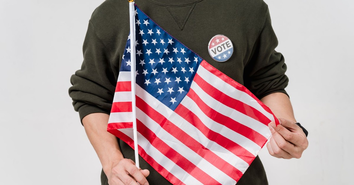 A man holding a USA flag and wearing a vote badge, symbolizing patriotism and democratic participation.