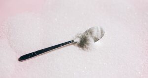A silver spoon nestled in a mound of white sugar on a pink background.