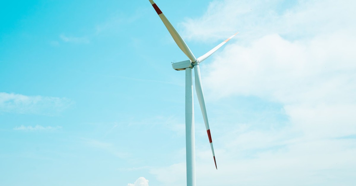 A wind turbine stands tall against a clear blue sky on a grassy field, symbolizing renewable energy.
