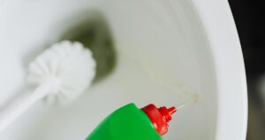 7 Ways To Remove Toilet Rings Fast (And Stop Them Coming Back) Top view of liquid detergent pouring from green plastic bottle in toilet bowl with toilet brush