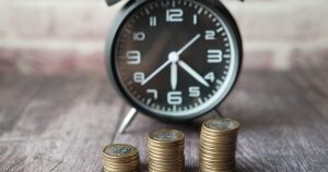 How Would Permanent Daylight Saving Impact Your State? Stacked coins and a classic alarm clock symbolize the value of time and money.