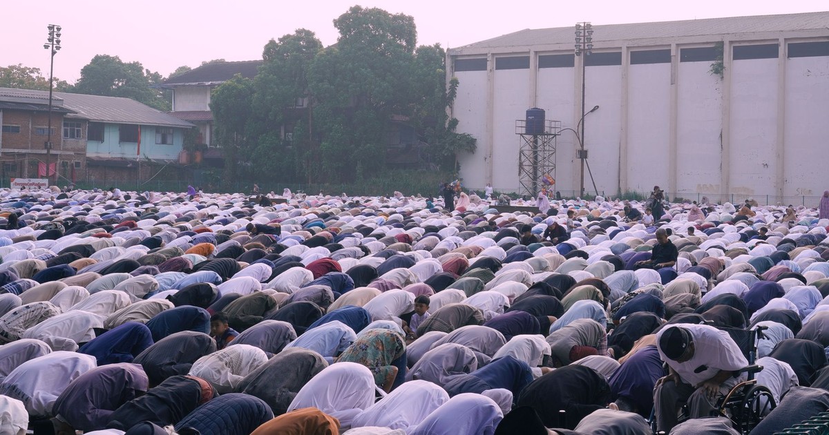 Large group of people gathered outdoors for prayer at dusk. Community, faith, and tradition are highlighted.