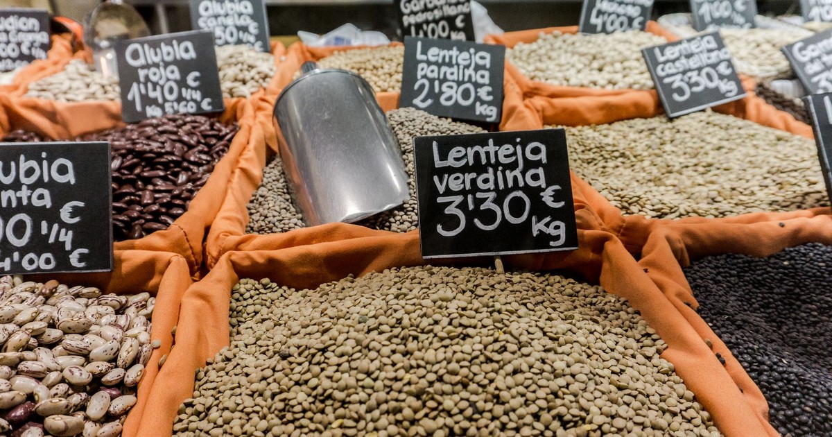 Close-up of multiple legumes in sacks at a market stall with price tags.