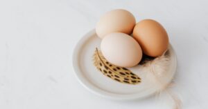 Three fresh eggs on a decorative plate with feathers on a white background.