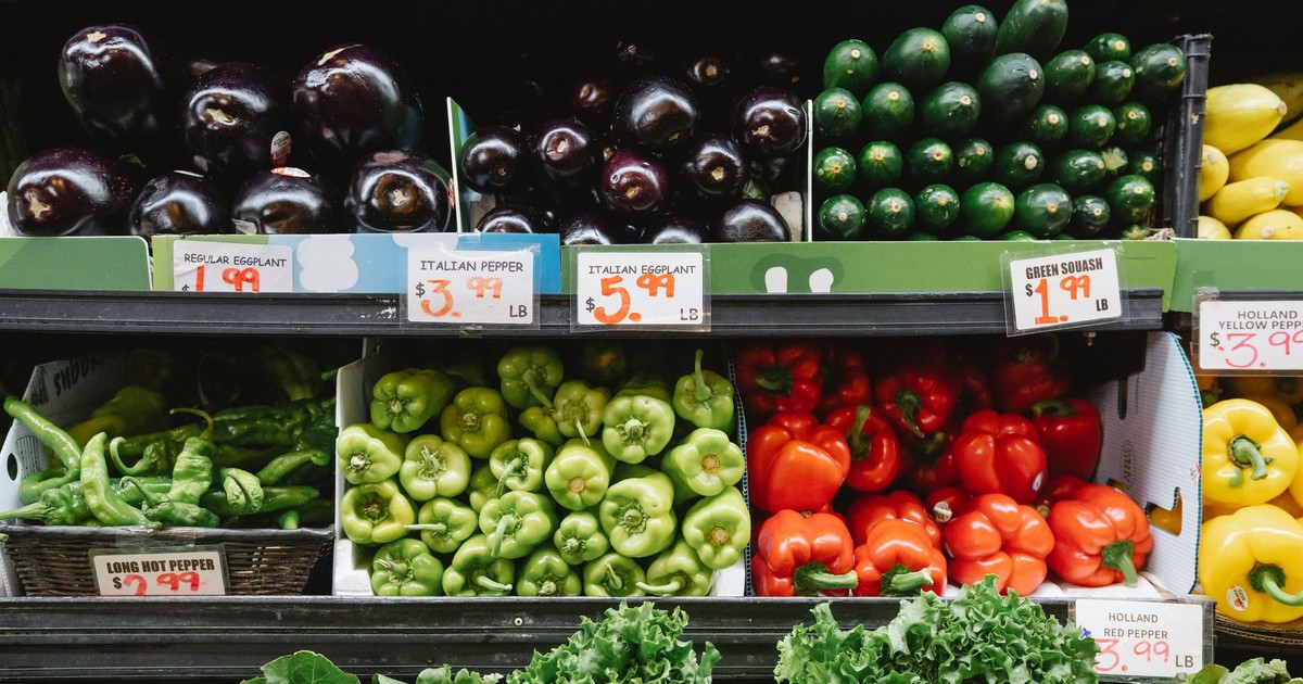 Colorful assortment of vegetables on display in a supermarket, featuring peppers, eggplants, and squash.