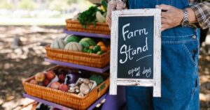 California Farmer Gives Away 125,000 Pounds of Nectarines After Marketing Company Allegedly Blocked Their Sale A farm stand showcases fresh fruits and vegetables in baskets, with a welcoming sign and rustic aesthetic.