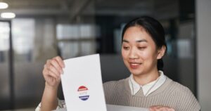Asian woman placing a ballot paper into a box during an indoor voting session.