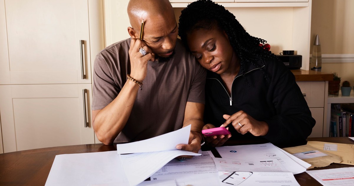 A couple sits at a table managing domestic finances, evaluating documents and using a smartphone.