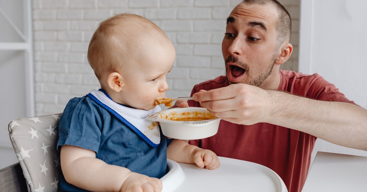 Loving father feeds baby in a high chair, bonding moment indoors.