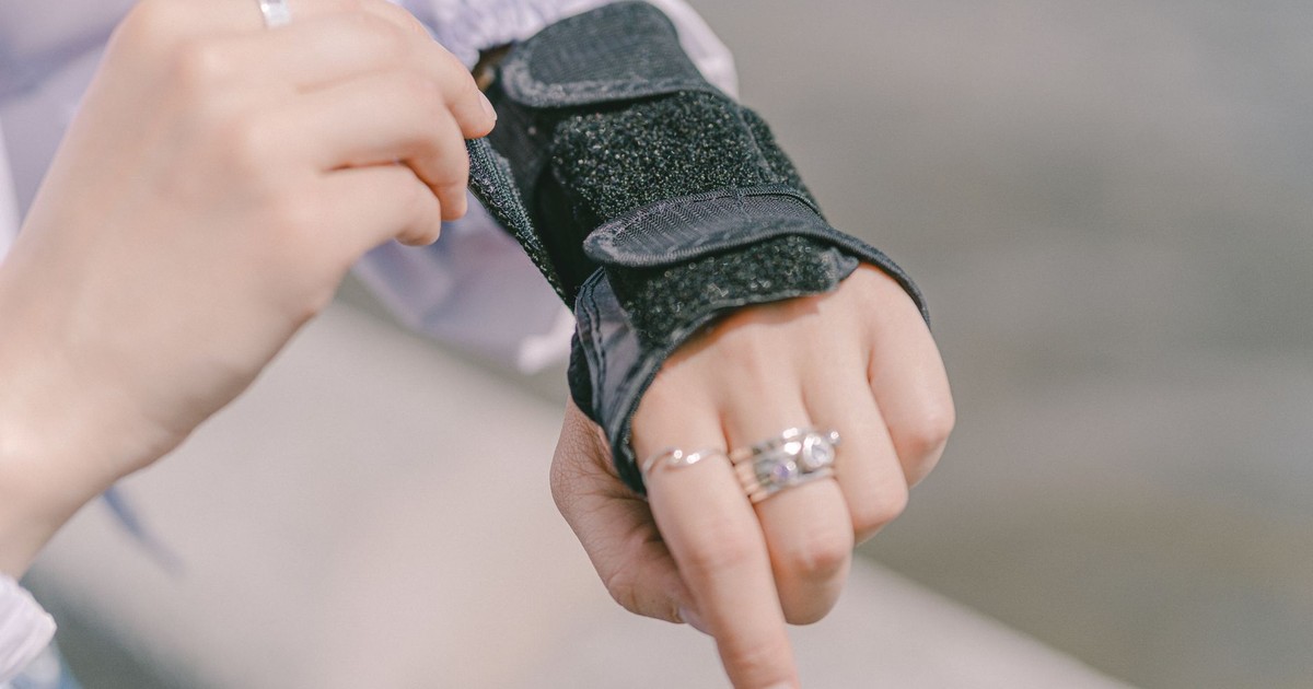 Detailed shot of a hand with rings adjusting a wrist brace, showcasing protection and style outdoors.