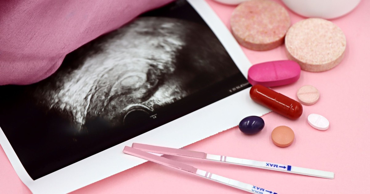 A closeup of pregnancy tests and an ultrasound with supplements on a pink background.