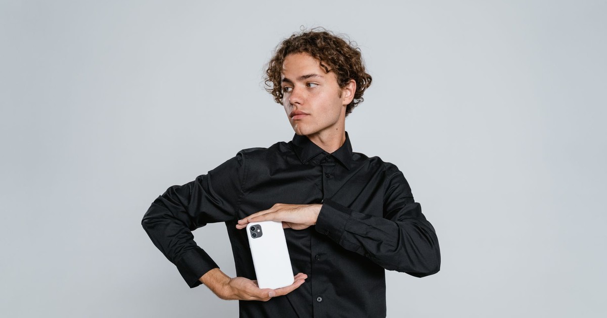Young man in black shirt holds smartphone in studio setting against white background.