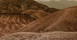 Two astronauts in spacesuits explore a barren, Mars-like landscape, suggesting space colonization.