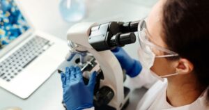 Scientist in protective gear examining samples with microscope in laboratory setting.