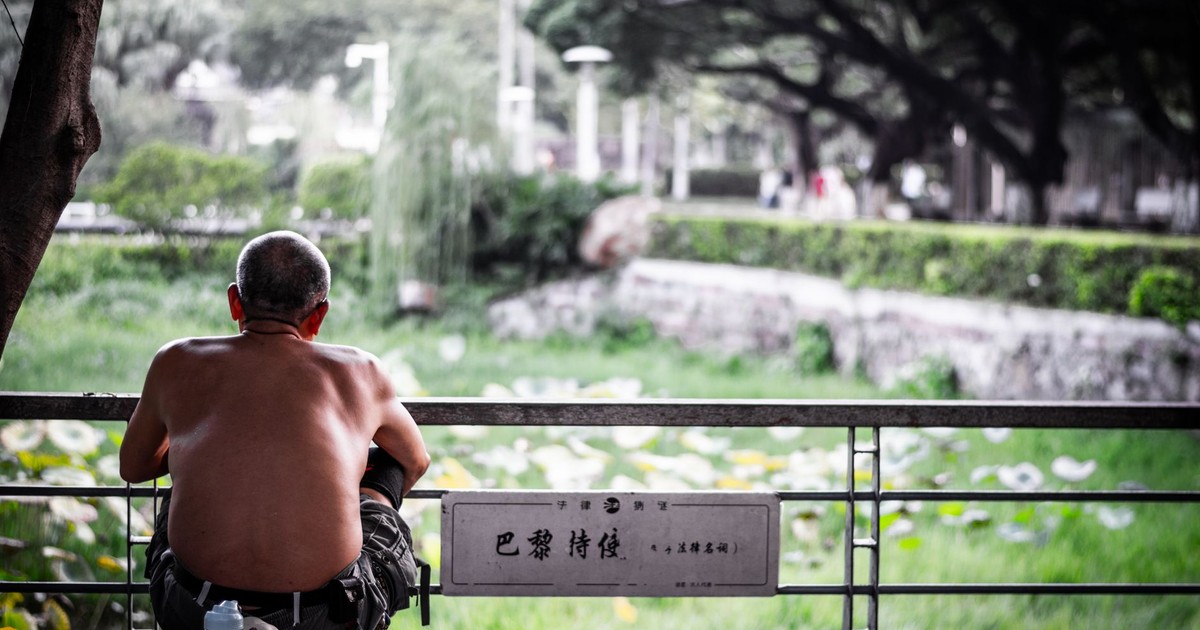 Shirtless man enjoying a peaceful moment by a pond in a lush park setting.